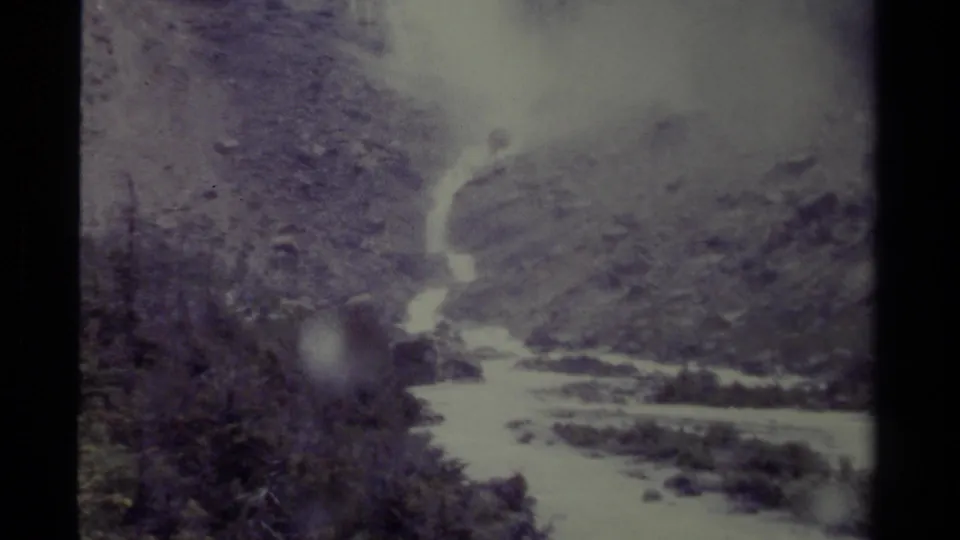 Faded 8mm view of a Canadian waterfall and stream, with evergreens and rocky terrain softened by age and exposure.