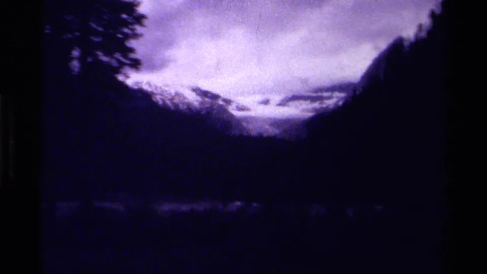 1979 Canadian 8mm view of a snowy mountain pass framed by dark wooded slopes and a clouded sky.