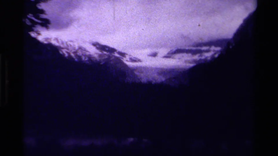 Purple-shifted 1979 Canada home-movie frame showing a wide snowy valley, dark tree line, and clouded mountain peaks.