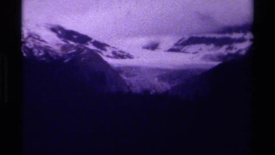 Late-1970s 8mm Canada frame of snowy peaks and a mountain pass, with dark slopes and visible aged-film texture.