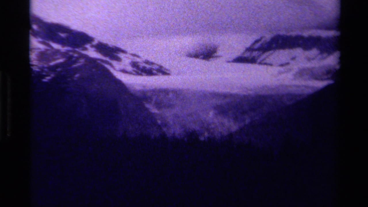 Snowy mountain slopes under low cloud with a dark treeline in the foreground.
