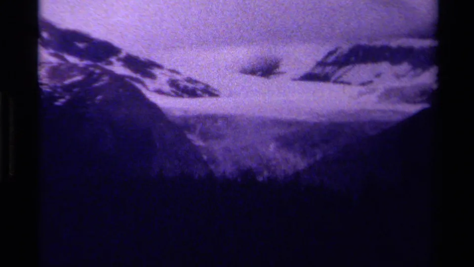 1979 8mm home-movie view of Canadian mountain snowfields, low cloud, and dark treeline with a purple film cast.