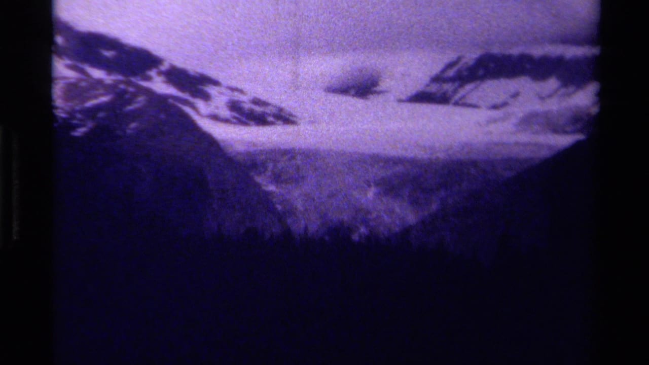 Canadian mountain landscape on 8mm film, with snowfields, low clouds, and a dark treeline under a purple-tinted sky.