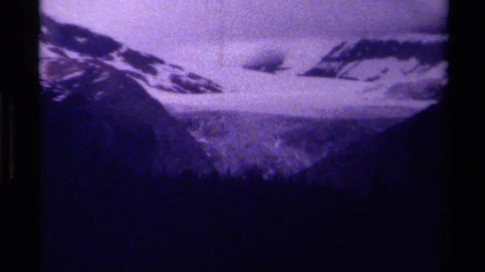 Canadian mountain landscape on 8mm film, with snowfields, low clouds, and a dark treeline under a purple-tinted sky.