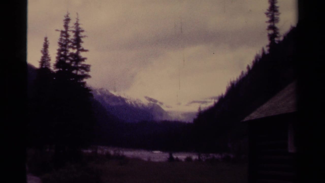 1979 Canada 8mm frame showing a shadowed mountain waterway, evergreen slopes, cloudy sky, and distant snow patches.