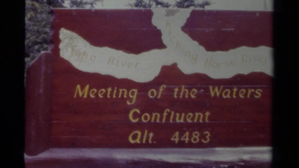 1979 Canada 8mm frame of the red Meeting of the Waters sign, with soft focus, gate edge, and water glare near the bottom.