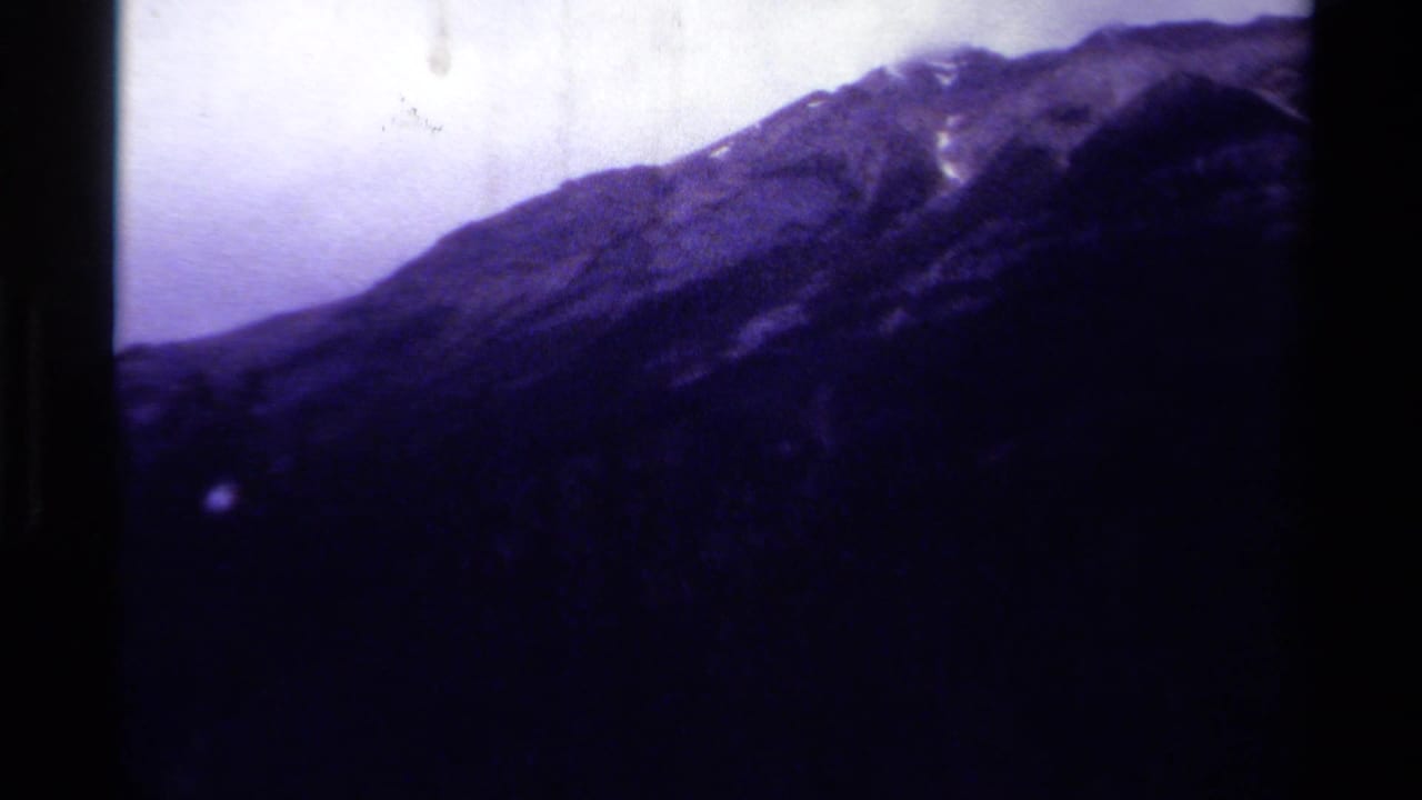 Purple-tinted mountain slope under a pale sky with dark film-frame edges.