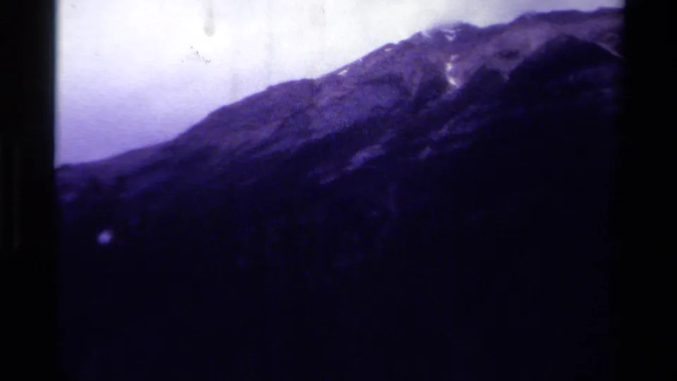 1979 Canadian 8mm frame of a distant mountain slope, pale sky, and heavy purple-blue film cast with visible gate edges.