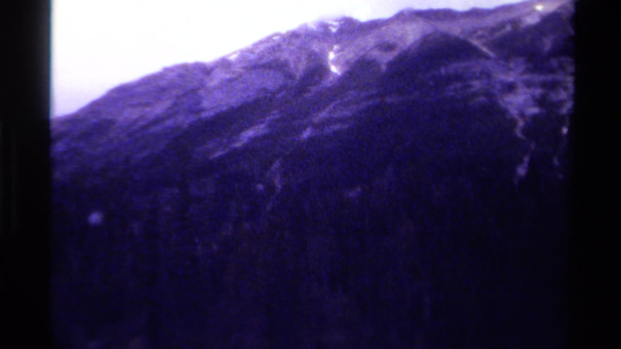 1979 Canadian 8mm view of a dark mountain ridge with pale snow streaks, soft focus, and strong purple-blue color shift.