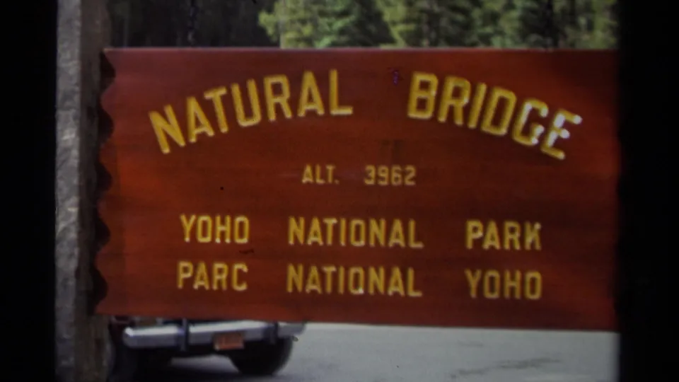 Close view of the Natural Bridge sign at Yoho National Park, Canada, with a partial period vehicle and forested background.
