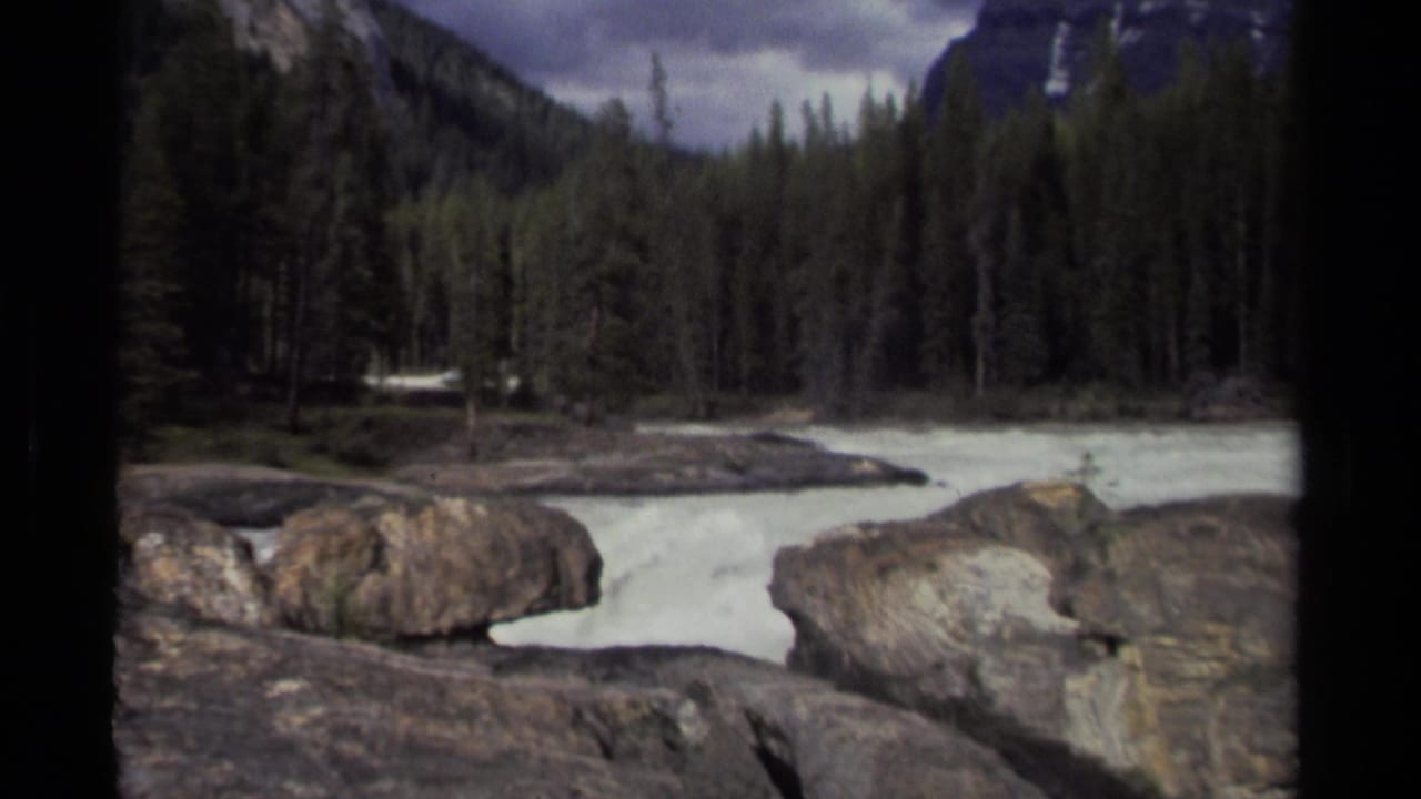 Rocky river channel with white water, forest, and steep mountain sides.