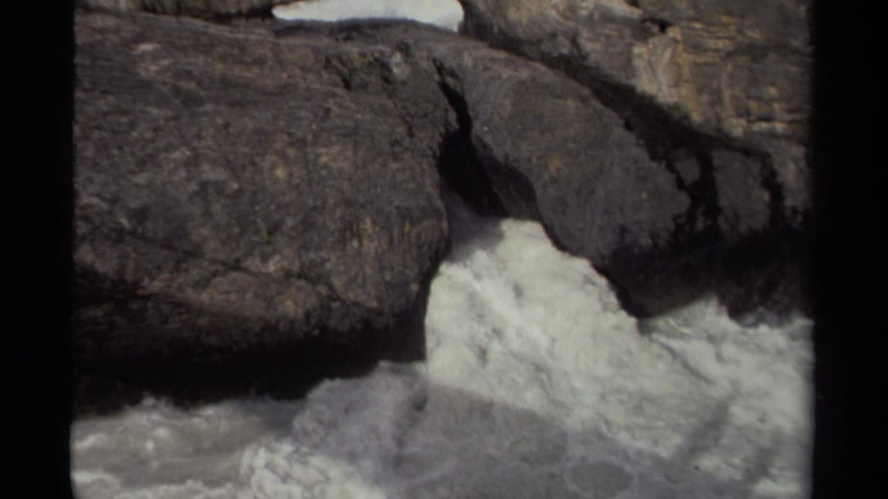 White rapids pour through a gap between heavy rock formations.