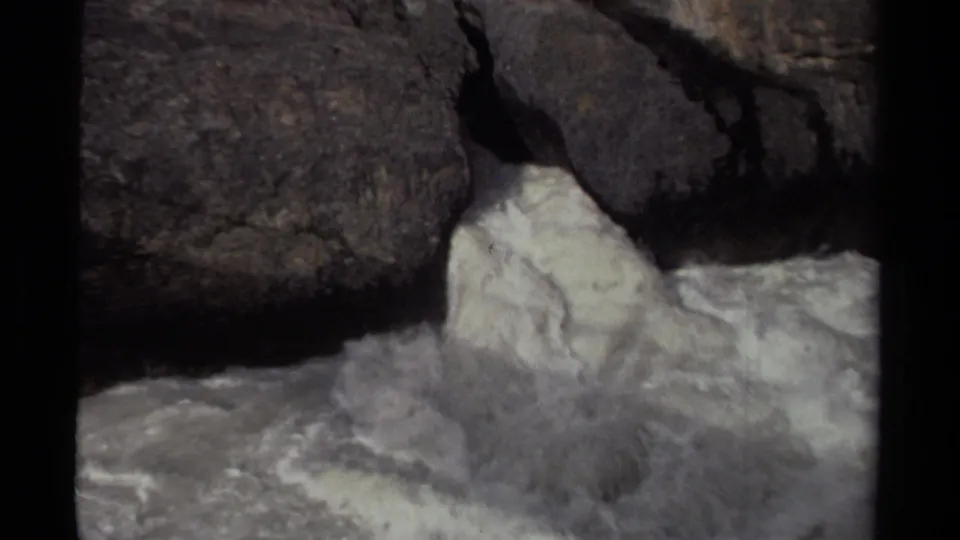 8mm archival frame from Canada showing churning white water moving around dark stone ledges.