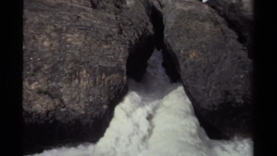 Vintage 8mm Canadian waterfall frame with turbulent water emerging from a narrow rock cleft.