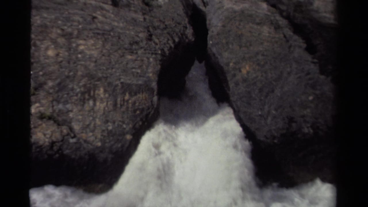 White water surges through a narrow gap between dark rocks.