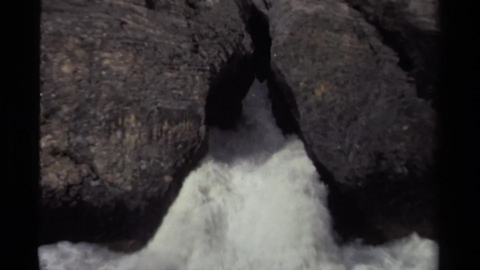 1979 Canada 8mm frame of foaming water forcing through a crevasse between large dark rocks.