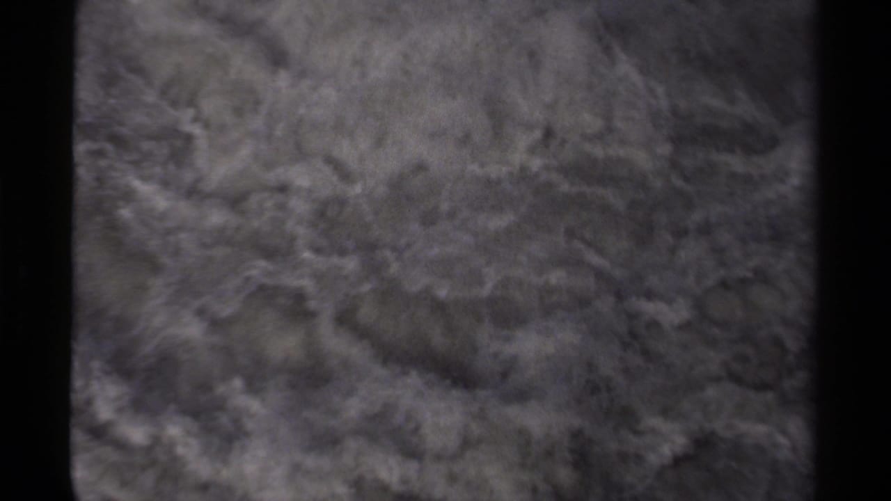 Foamy river water rushing past dark rocks in a soft, grainy frame.