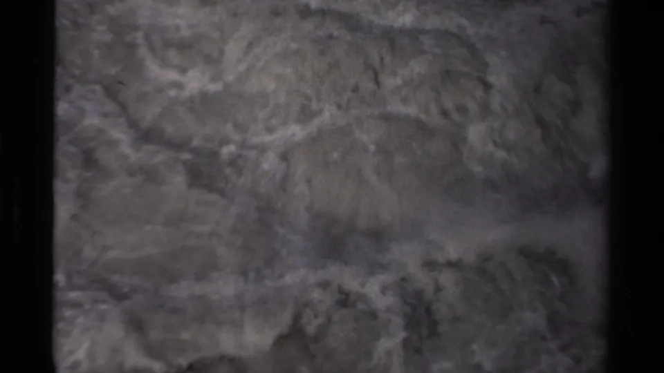 Soft 8mm view of churning Canadian river water, with pale foam patterns and dark bank edges.