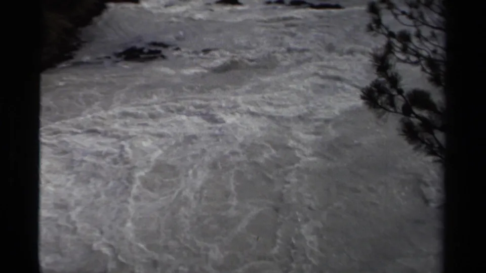 1979 Canadian home-movie frame of foamy rapids, small rocks, and dark tree branches at the river edge.