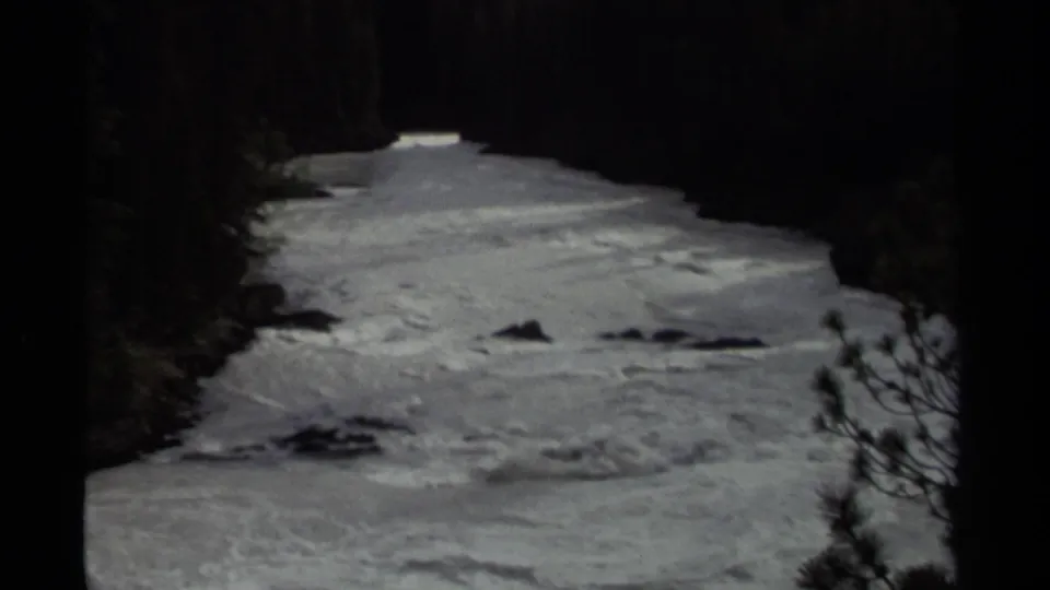 1979 Canadian 8mm frame of white water moving through a shaded forest river, with rocks breaking the surface.