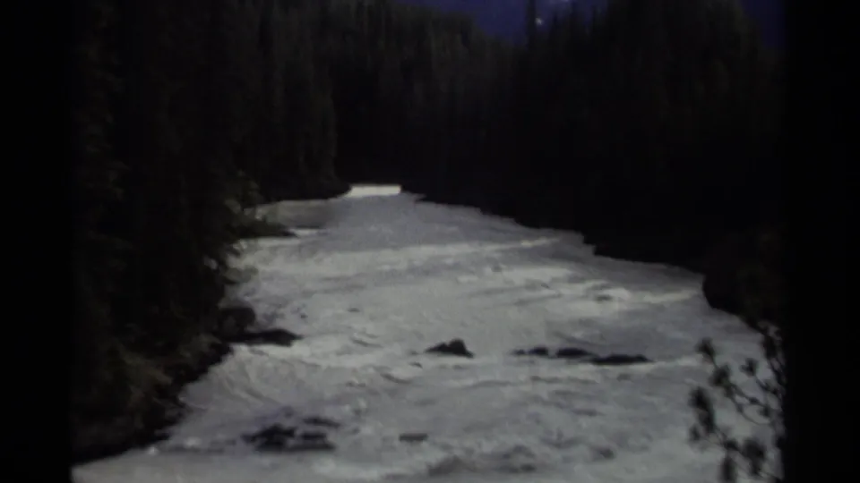 1979 Canadian 8mm frame widening to show a forest river corridor with white water and evergreen banks.