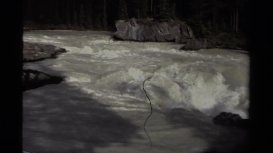 1979 Canadian 8mm view of turbulent rapids below a rocky outcrop, with evergreen forest beyond and visible film wear.