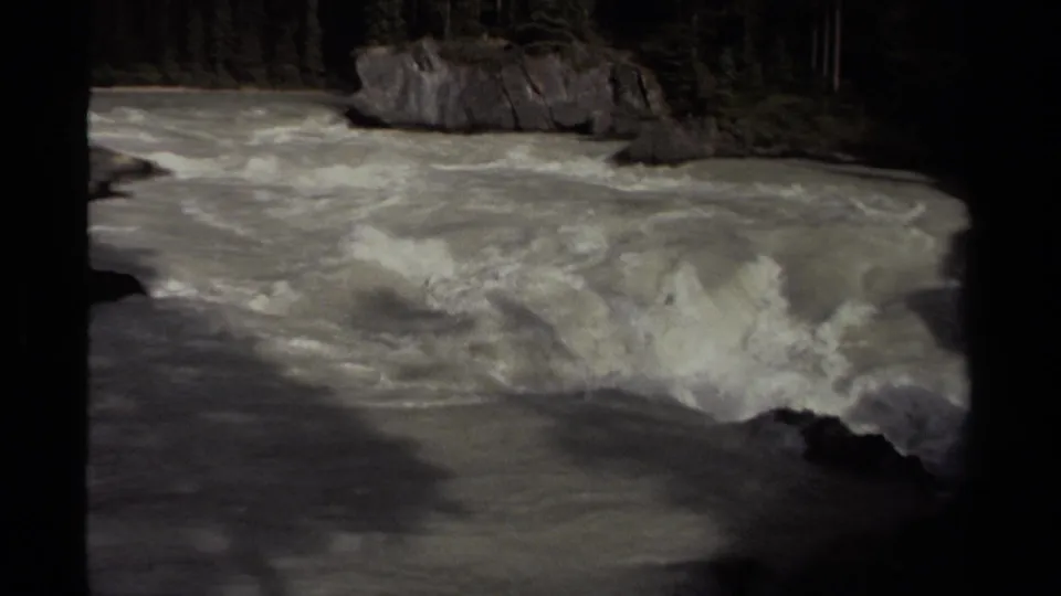 1979 Canadian 8mm frame of foamy whitewater moving through a rocky, forested river channel.