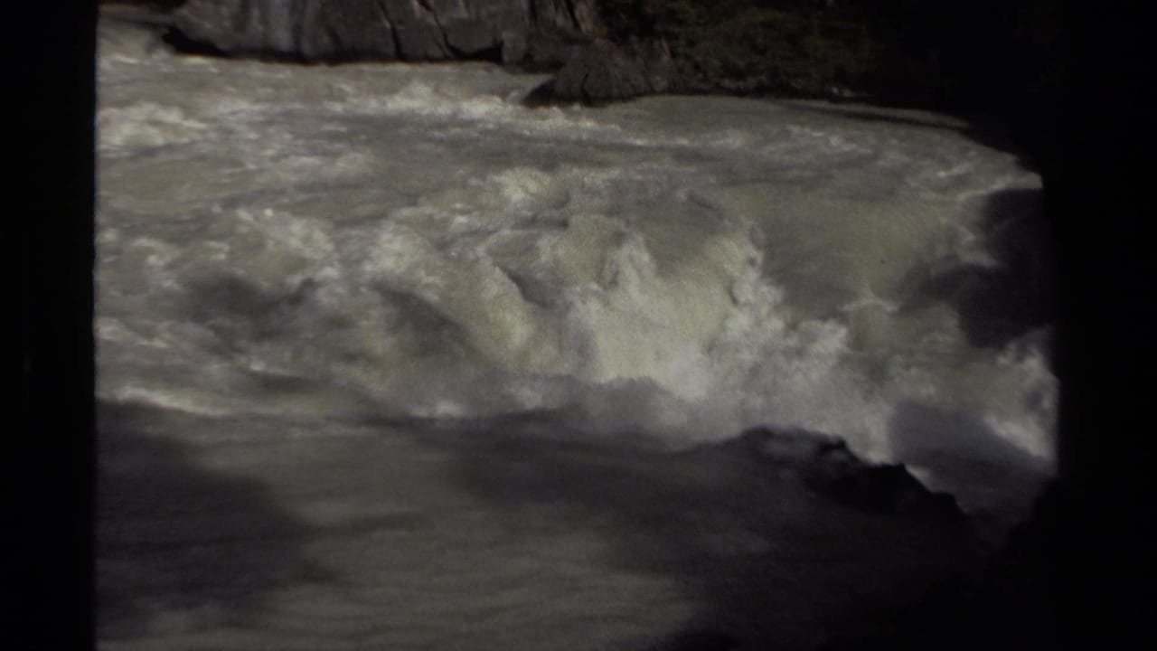 1979 Canadian home-movie frame showing turbulent river foam and rock edges in a forested canyon setting.