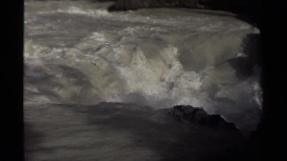Closer 8mm view of a Canadian river cascade, with foamy water pushing around dark rocks.