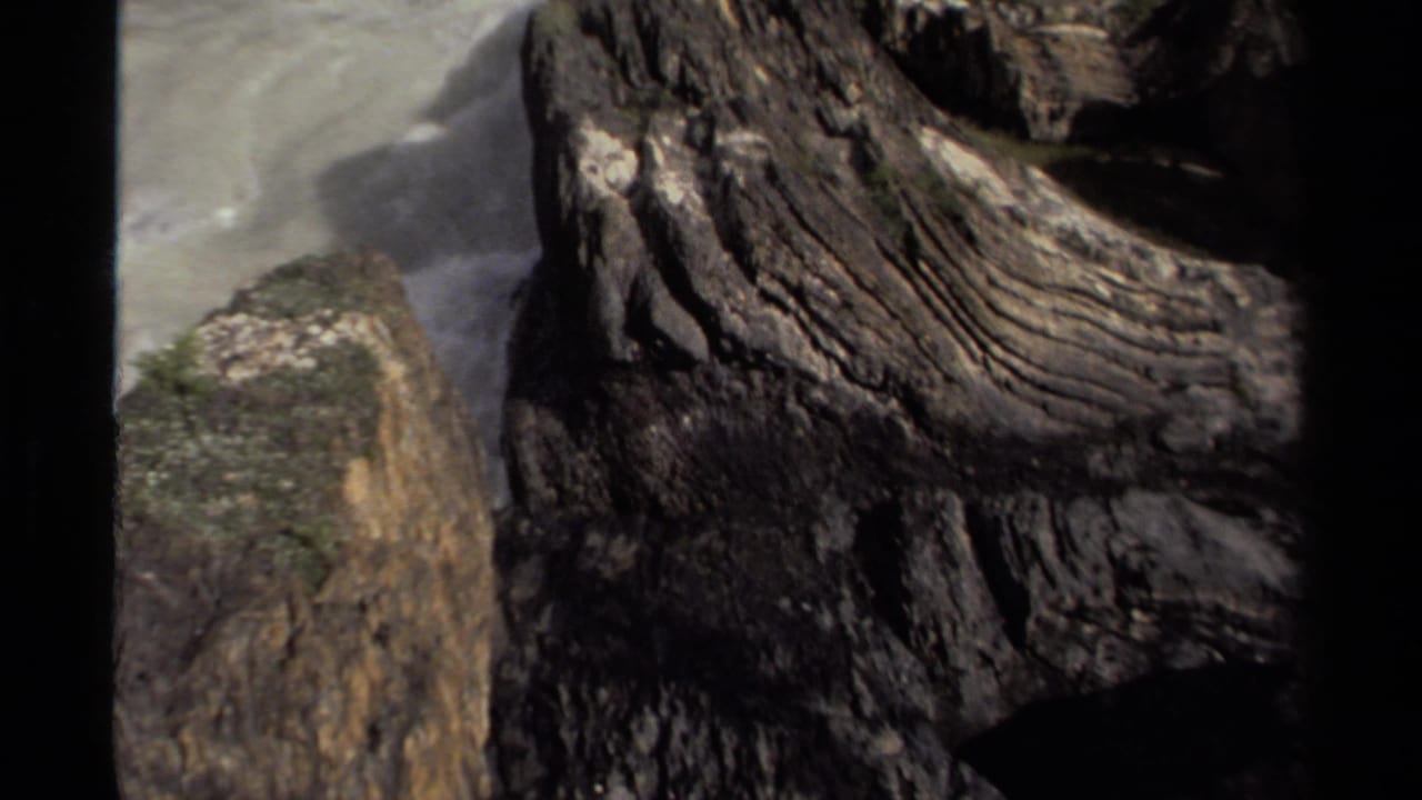 1979 Canada 8mm frame with striated rock face, wet cliff edge, and blurred waterfall spray behind it.