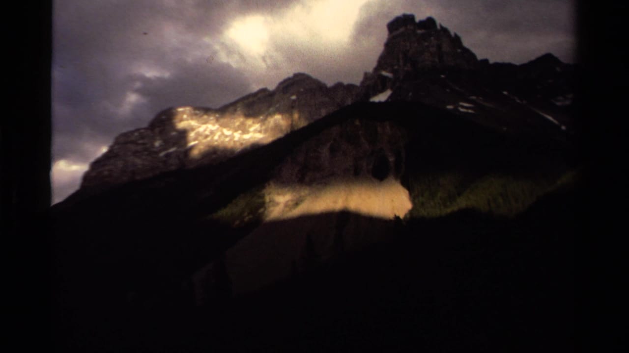 Jagged mountain peaks under dark clouds with sunlight on rocky slopes.