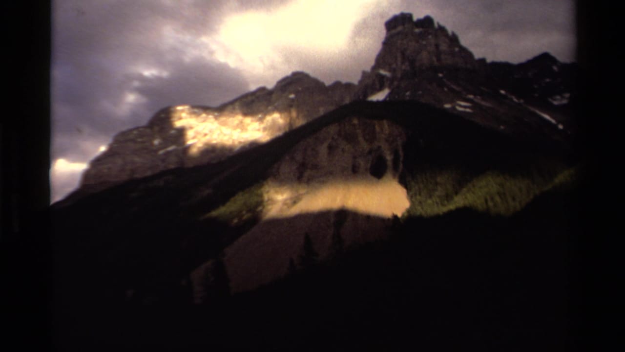 Mountain ridge and peak beneath a bright break in dark cloud cover.