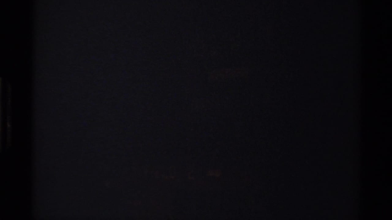 Start of the 1979 8mm clip, largely dark, with a partial red directional sign and forest background beginning to enter the frame.
