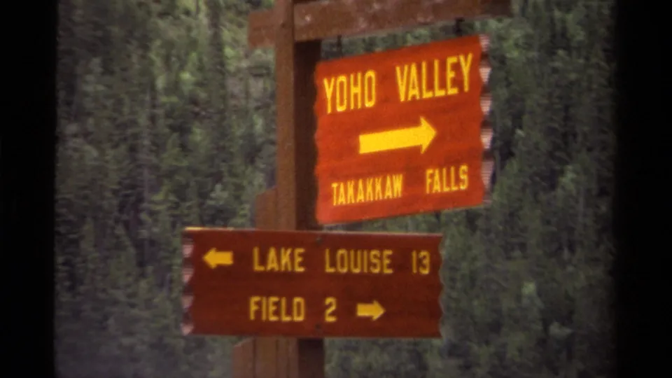 Final frame holds on the Canadian park signpost, with yellow arrows and place names visible against a dark green forest.