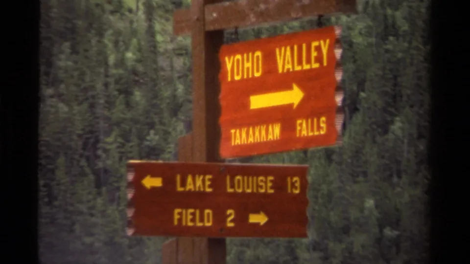 1979 Canada 8mm frame showing wooden park-style signs for Yoho Valley, Takakkaw Falls, Lake Louise, and Field against forest.