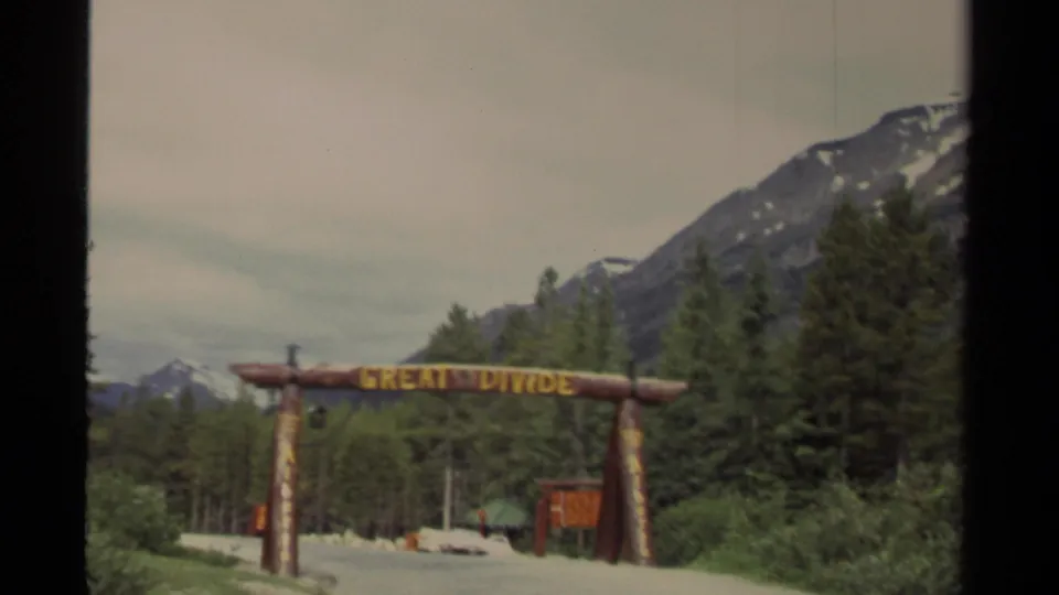 1979 Canada 8mm frame showing the Great Divide entrance archway against evergreens and snow-patched mountain slopes.