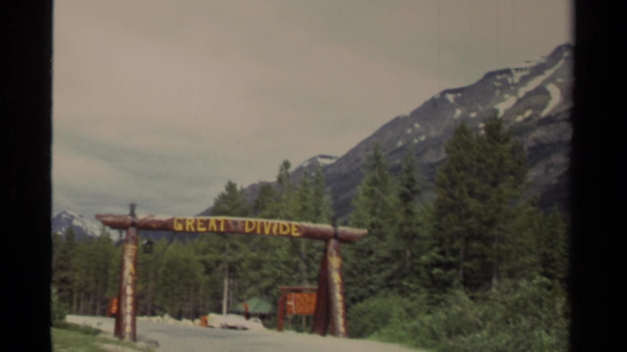 1979 Canada home-movie frame showing a rustic Great Divide log sign before forested mountain slopes.