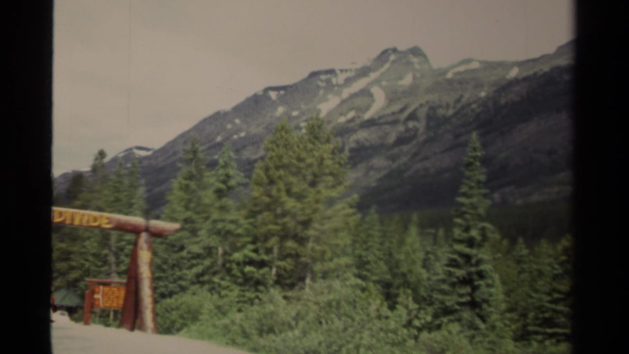 Roadside Great Divide sign partly visible with forest and layered mountain slopes behind.