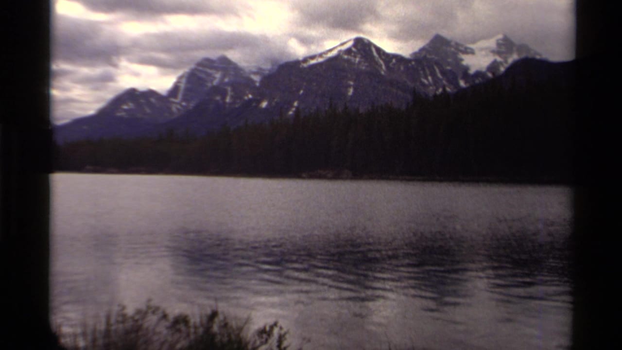 Canadian 1979 home-movie view of snowy mountain peaks above a dark forest and broad lake surface.