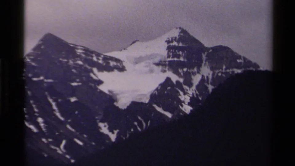 1979 Canadian 8mm frame showing a snow-laden mountain face, dark ridgelines, and shadowed lower terrain in soft vintage color.