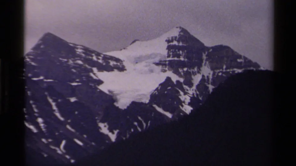 1979 Canadian 8mm frame of snow-capped peaks and a dark foreground slope beneath a muted, overcast sky.