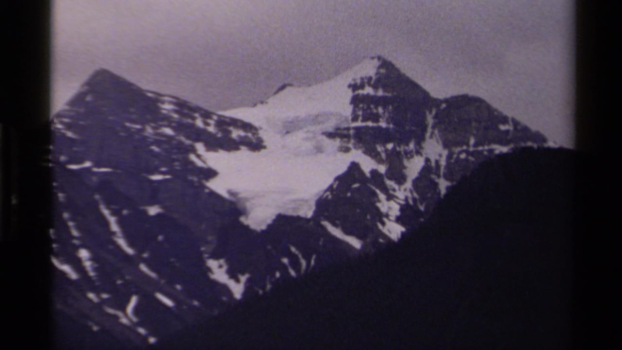 Snow-capped mountain peaks under a cloudy sky with dark slopes below.