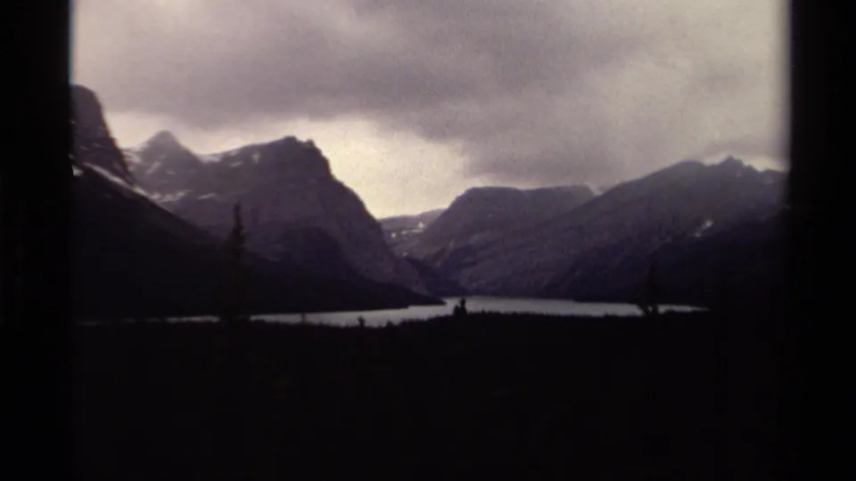 1979 Canadian 8mm frame showing a lake receding between steep mountain slopes, with dark forest in the foreground.