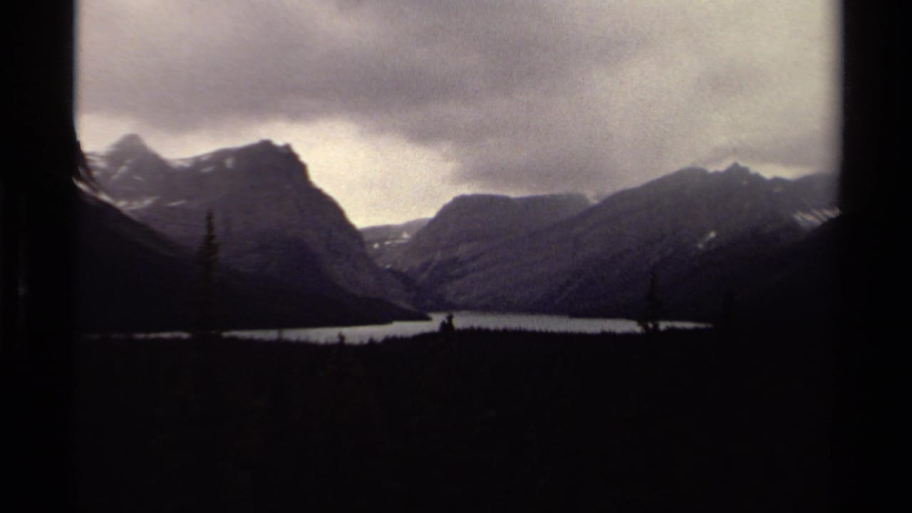 Misty alpine lake between dark mountain ridges under an overcast sky.