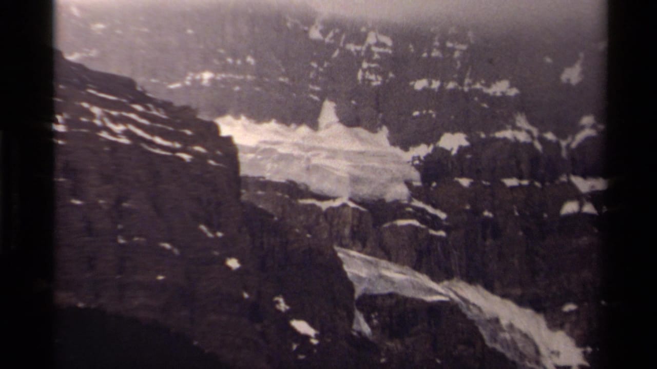 1979 Canadian 8mm view of rugged mountain cliffs with patches of melting snow and fog across the upper slope.
