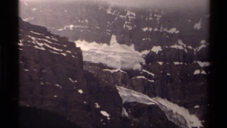 1979 Canadian 8mm view of rugged mountain cliffs with patches of melting snow and fog across the upper slope.