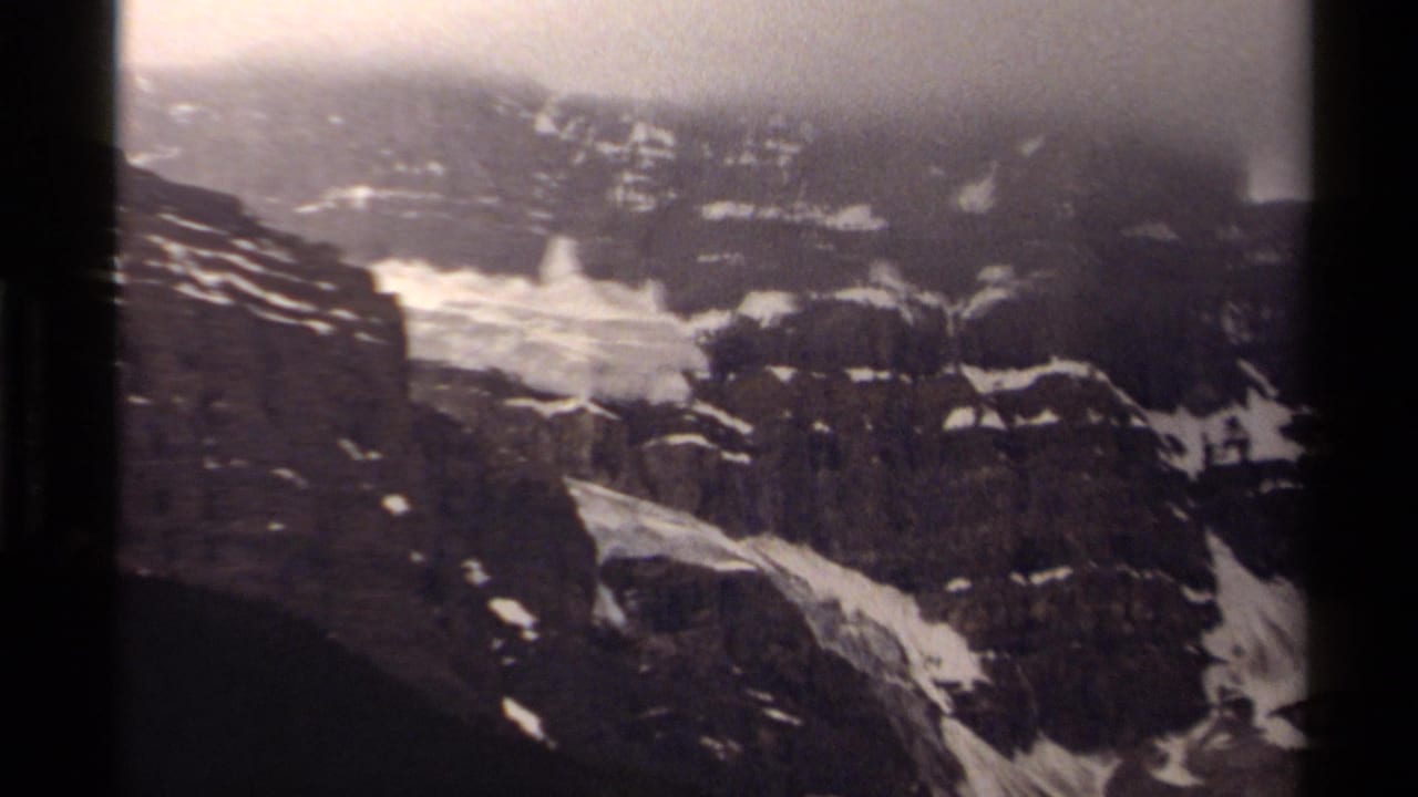 A Canadian alpine slope on 8mm film, showing dark rock faces, pale snow channels, and heavy fog near the ridge.