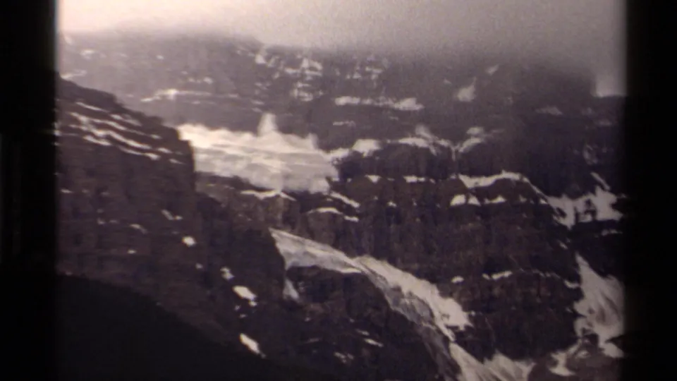 A Canadian alpine slope on 8mm film, showing dark rock faces, pale snow channels, and heavy fog near the ridge.