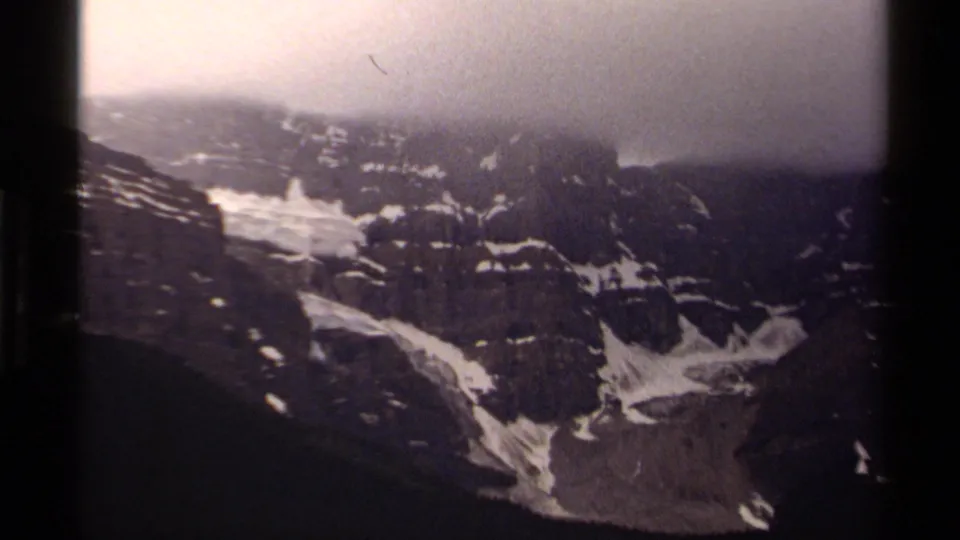 1979 8mm view of a Canadian alpine cliff face, with melting snow patches and fog softening the ridge line.