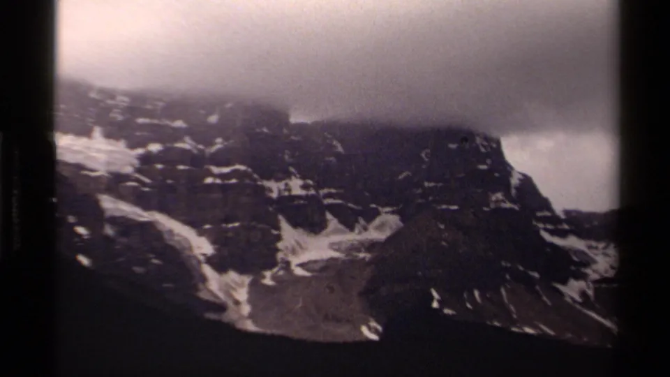 1979 Canadian 8mm view of jagged rock faces, lingering snow, and dense cloud over the mountain top.